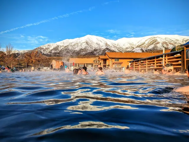 Crystal Hot Springs outdoor pool with people soaking, steam rising, and snowy mountains near Honeyville Utah in the background.