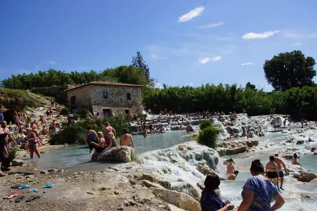 Many visitors enjoying the tiered hot spring soaking pools and stone building at Cascate del Mulino in Saturnia, Italy.