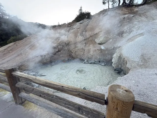 Milky hot spring mud pool encircled by a wooden fence with steam and rocky hillsides at Sulphur Works, California.