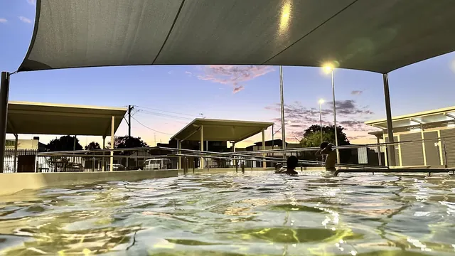 Two children playing in the warm waters of Collarenebri Bore Bath with surrounding shade structures at dusk in New South Wales.