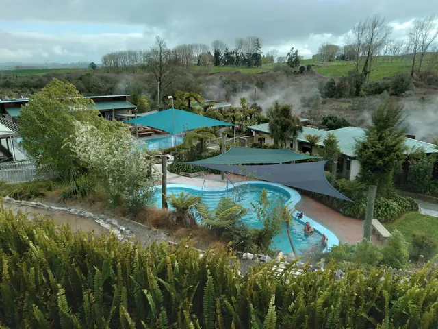 Multiple steaming outdoor hot spring pools at Waikite Valley Thermal Pools visible with shaded areas and green trees in Rotorua, New Zealan.