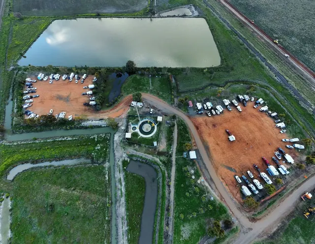 Aerial view showing the circular hot spring and surrounding parking area with many vehicles near green fields at Burren Junction Artesian B.