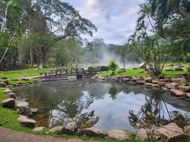 Natural outdoor hot spring pool surrounded by lush green trees and steam rising from the water near Lampang, Nan, Thailand.