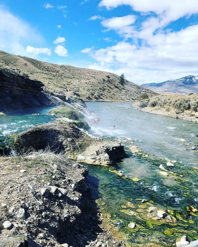 Hot spring river pools with natural steam rising and people soaking near rocky banks at Boiling River Hot Springs by Mammoth Hot Springs, W.