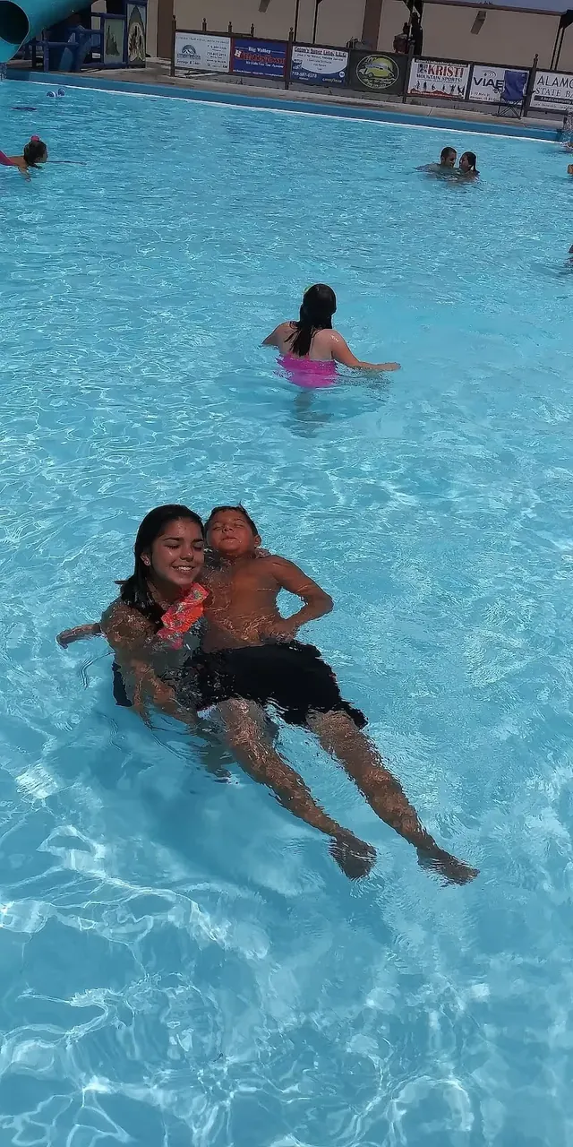 A woman holds a child while wading in the large blue pool at Splashland Hot Springs located in Alamosa, Colorado, on a sunny day.