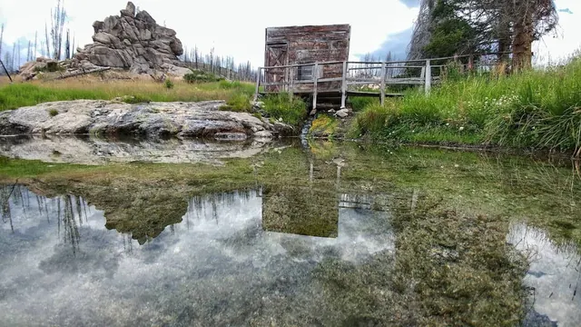 Natural hot spring pool with mirroring water and a shed at dash creek hot springs idaho