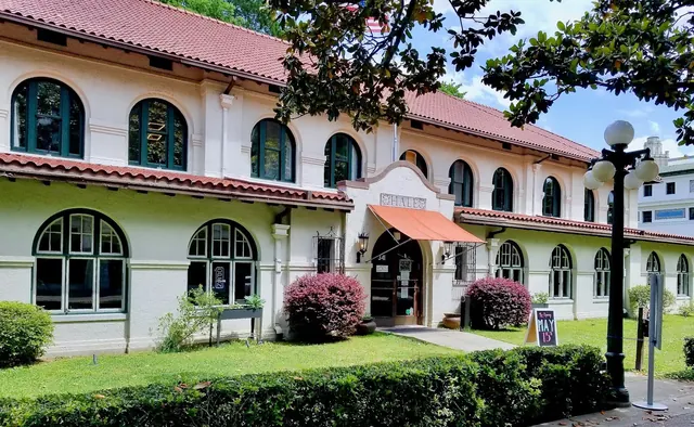 Two-story historic building with arched windows and red tile roof surrounded by green bushes in Hot Springs, Arkansas.