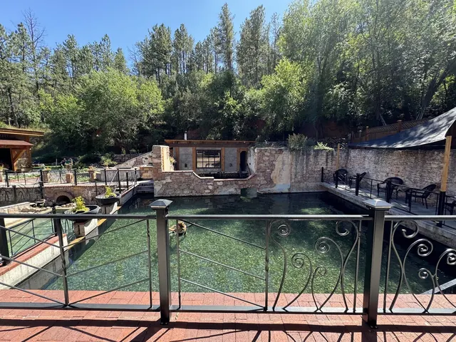 Large fenced natural hot spring pool at Moccasin Springs in Hot Springs South Dakota with clear water and surrounding trees on a sunny day.