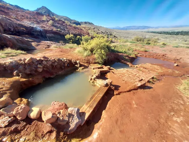 Natural stone soaking pools filled with murky water at Red Hill Hot Springs near Monroe, Utah, surrounded by red soil and desert scrub.