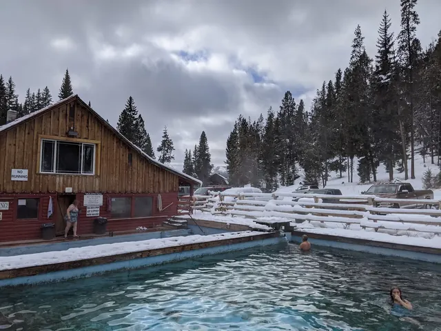 Outdoor soaking pool with steaming water at Elkhorn Hot Springs in Polaris, Montana, surrounded by snow and pine trees.