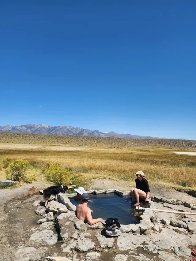 Two people soaking in Shepherd Hot Springs pool surrounded by rocks with dog and mountain view near Mammoth Lakes california.