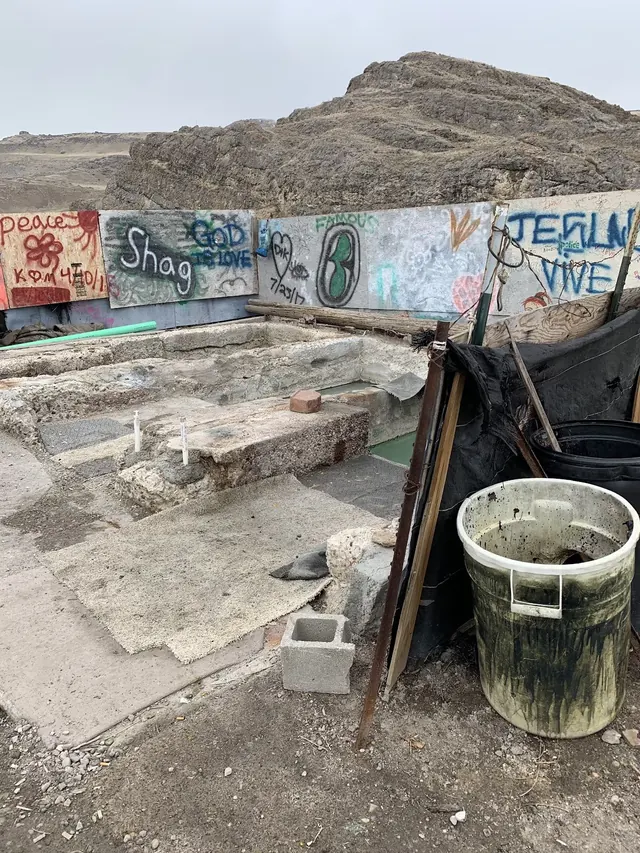 Old Indian Hot Spring features stone soaking pools surrounded by graffiti-covered panels and scattered outdoor items in a dry mountainous a.