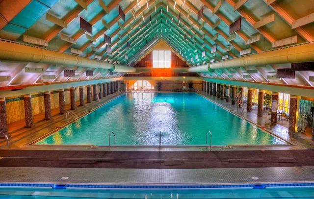 Interior view of a large indoor hot spring pool with high pitched green ceiling and light streaming through end windows in Montana.