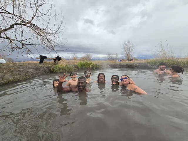 Group of people with mud masks smiling and waving while soaking in the steamy outdoor pool at Inlet Hot Springs near Saratoga Springs Utah.