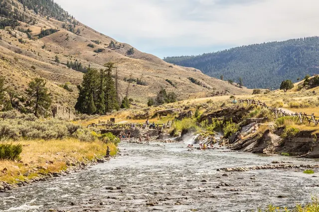 Steam rising over people soaking in hot spring pools surrounded by rocky banks and dry hills at Boiling River Hot Springs Montana.