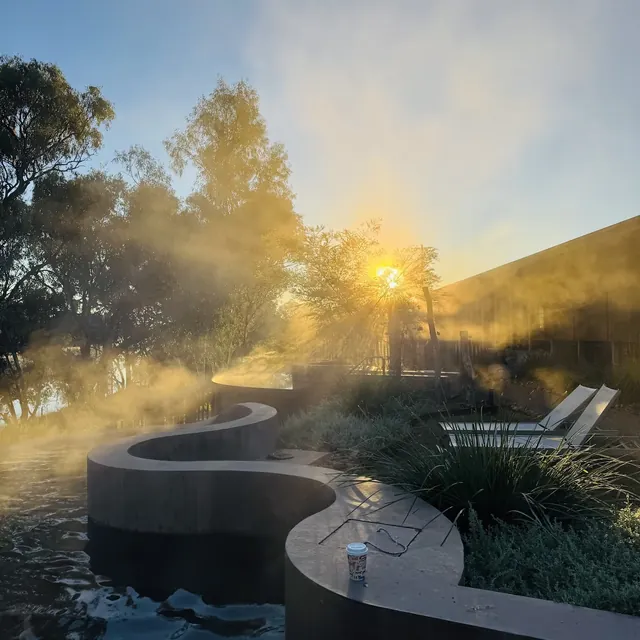 Indoor hot spring soaking pool with white tiles and stone flooring beneath a round skylight allowing natural sunlight in at Cunnamulla Hot.
