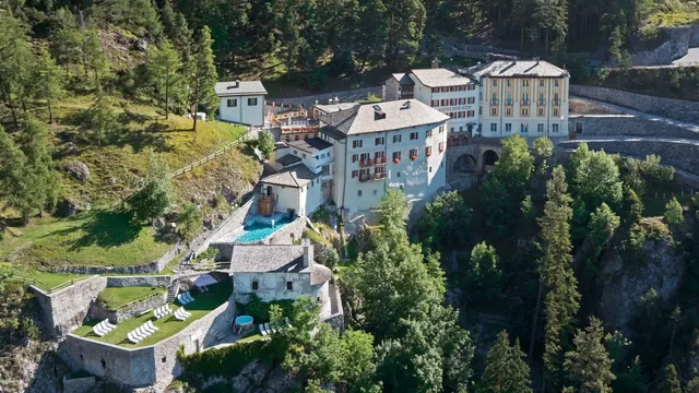 Aerial view of historic stone buildings and multiple connected pools surrounded by dense green forest at QC Terme Bagni Vecchi near Valdide.
