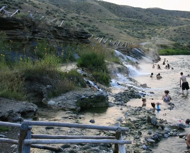 Visitors walking and soaking in rock-lined natural pools beside a flowing river at Boiling River Hot Springs near Gardiner Montana.