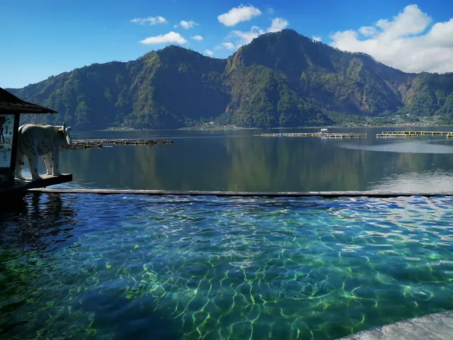 Clear infinity style hot spring pool reflecting sunlight with a mountain lake view near Kintamani Bali Indonesia.