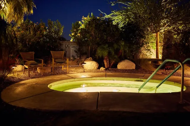 The Spring Resort & Spa outdoor hot spring pool lit at night surrounded by chairs and tropical plants in Desert Hot Springs California.