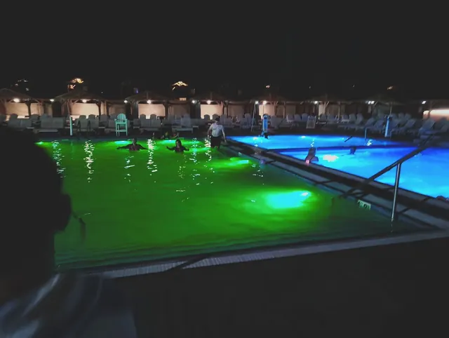 Night view of Kah-Nee-Ta Hot Springs soaking pools with glowing green and blue underwater lights and several bathers under soft ambient lig.