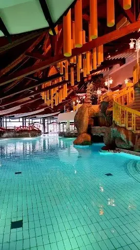 Indoor mineral pool at Taunus Therme with glowing warm water, wooden beams, large windows, and bright orange hanging lights.