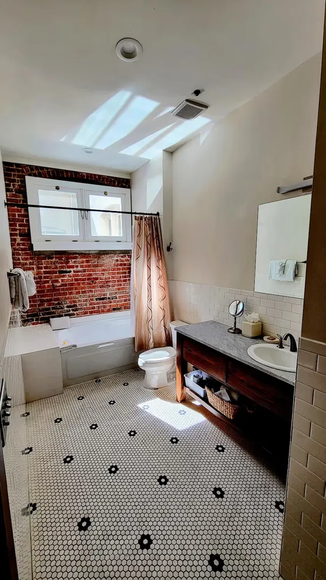 Bathroom with white hexagonal tile floor, brick accent wall behind bathtub, and wooden vanity in Hot Springs, Arkansas.