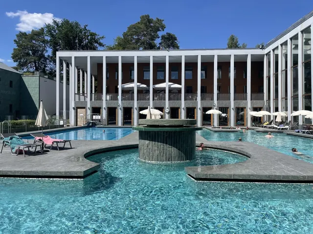 Outdoor pool area at SaarowTherme in Bad Saarow Germany with lounge chairs, umbrellas, and a modern building on a clear sunny day.