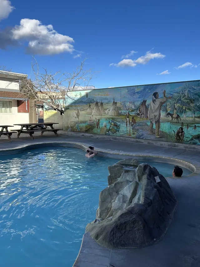 Two people relaxing in translucent blue water of Spa Hot Springs Motel and Clinic mineral pool in White Sulphur Springs, Montana.