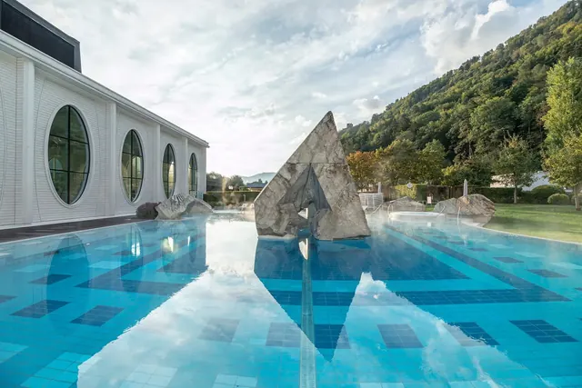 Steaming outdoor pool at Tamina Therme surrounded by green lawn and trees under cloudy sky near Bad Ragaz Switzerland.