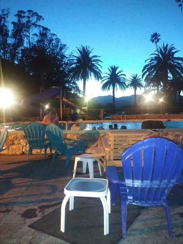 Evening view of Avila Hot Springs outdoor pool area with illuminated water slides, palm trees, and chairs near Avila Beach California.