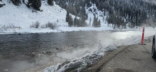 Steam rising from Boat Box Hot Spring beside a roadside near Stanley, Idaho, with snow-covered scenery and a vehicle nearby