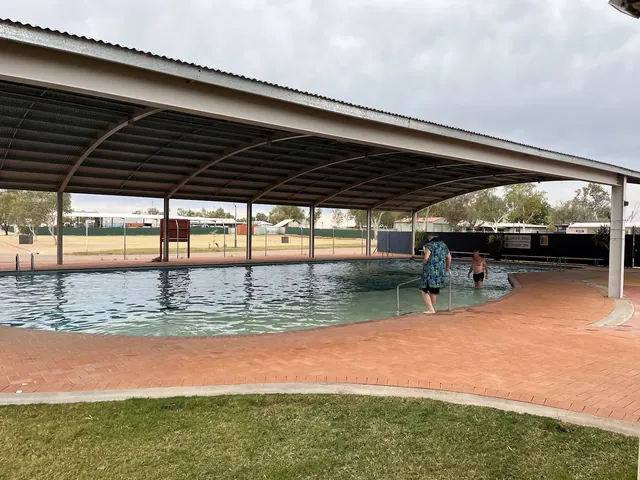 People enjoying water in covered swimming pool at Bedourie Artesian Spa and Aquatic Centre with open surroundings and green grass poolside.