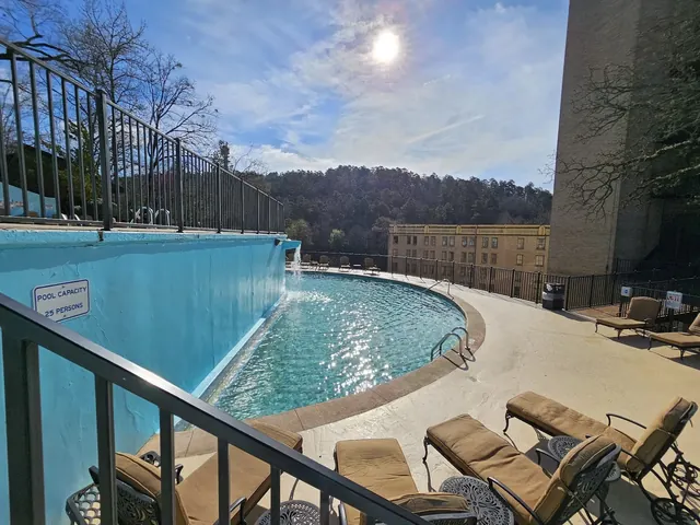 Outdoor hot spring pool at Arlington Resort Hotel & Spa in Hot Springs Arkansas with lounge chairs and a blue wall under sunlight.